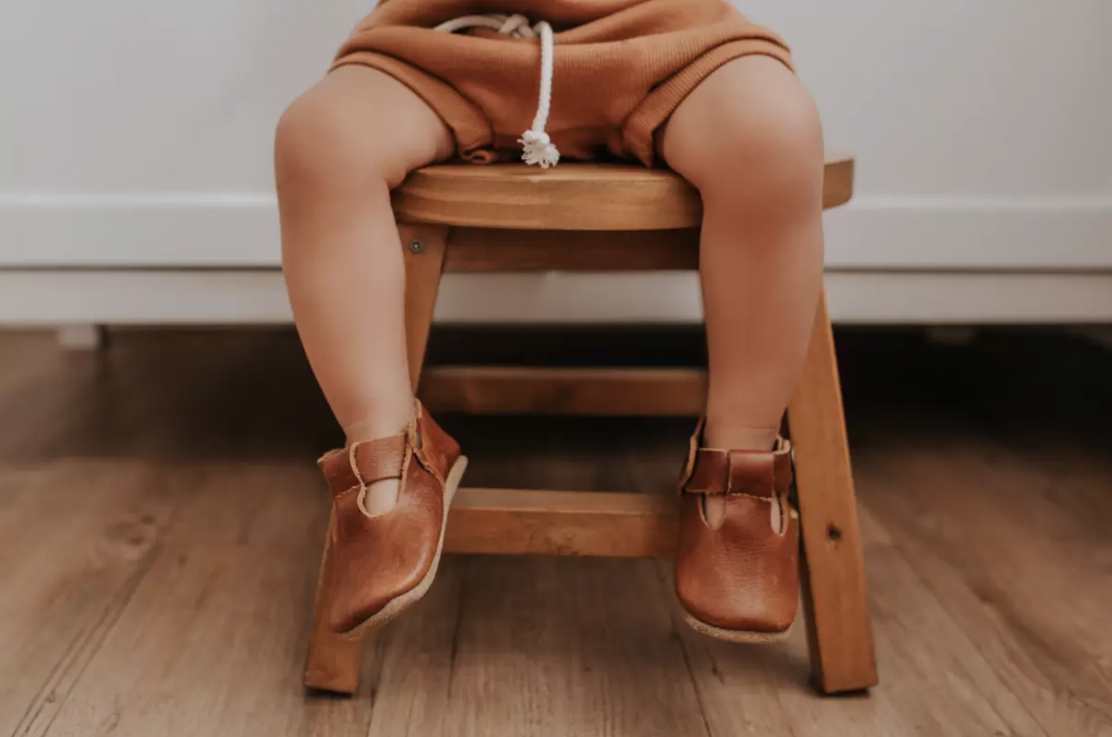 Criança sentada em banquinho, mostrando um sapatinho marrom nos pés - Just Real Moms