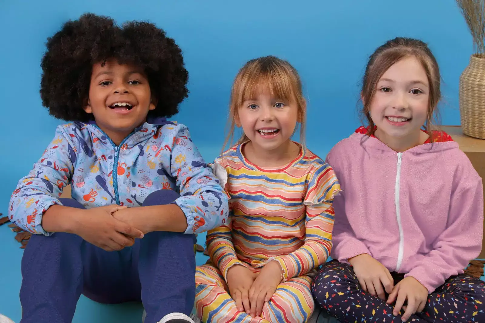 3 crianças modelos sentadas posando com a nova coleção de inverno da marca infantil Petit Pelicano - Just Real Moms